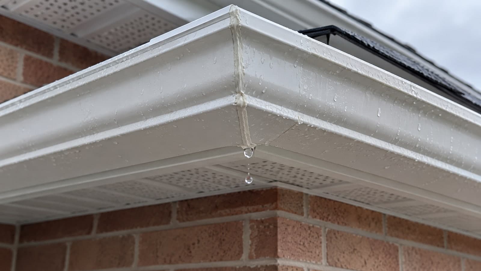 Drip forming at the sealed corner joint of a new white aluminum eavestrough under fresh soffit